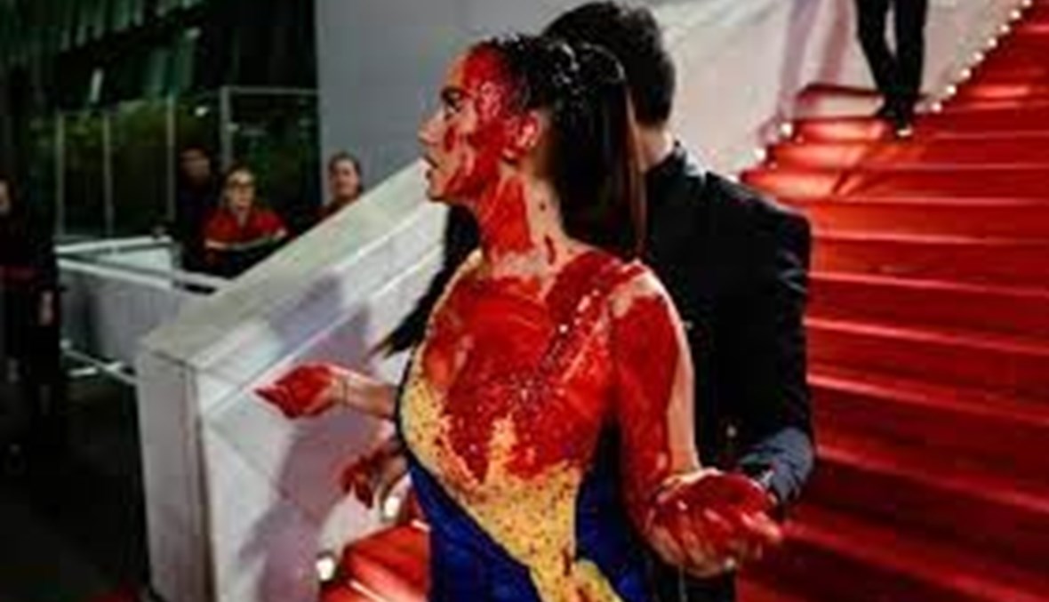 مرتديةً فستاناً بألوان العلم الأوكراني.. امرأة تسكب على نفسها الدماء في مهرجان كان